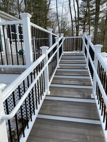 Outdoor staircase with white railings, black balusters, and gray wooden steps.