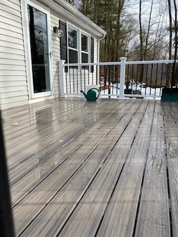 Wet, gray composite deck with a green watering can on it next to a house with black shutters.
