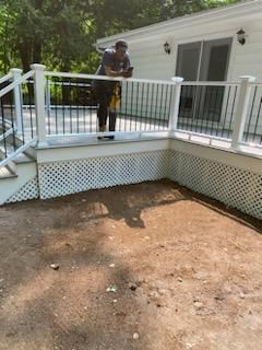 Person on a deck overlooking a dirt area, a white house and railing in the background.