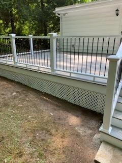 White deck with lattice skirting, black railings, and steps, in a yard.