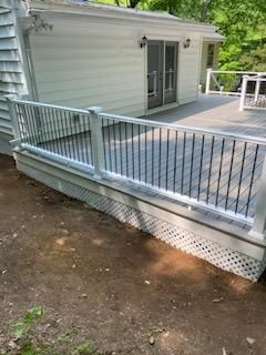 Deck with white railing and lattice skirting, gray composite decking, and a sliding glass door.
