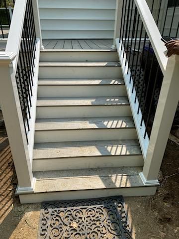White stairs with black railings lead up to a deck. A decorative mat rests at the base.