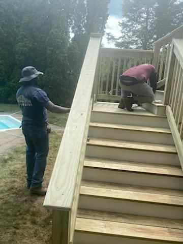 Two men building wooden deck stairs. One measures, the other works. Outdoors, near a pool.