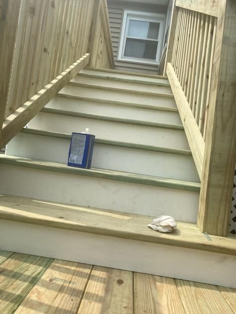 Wooden outdoor staircase with light gray steps and railing, solvent and rag on stairs.