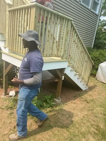 Man walks by a newly built wooden deck with stairs. A person is partially visible on the stairs.