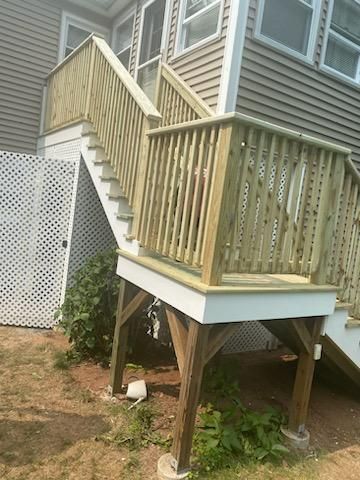 Wooden deck with stairs leading to a house. Greenish-brown railings and tan siding on the house.