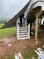 Workers installing a canopy over outdoor stairs. Brown tarp, white railing and steps, green lawn.