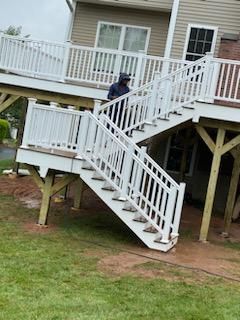 Person walking down white outdoor stairs attached to a two-story house with a wooden deck and green yard.
