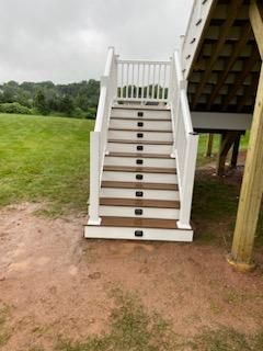 White-railed stairs descend from a deck to a grassy yard. Each step has a dark-colored light.