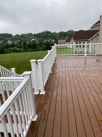 Wet wooden deck with white railing overlooking a green lawn and houses under an overcast sky.