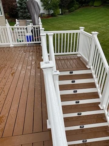 Wooden deck with white railings and steps. Brown deck boards with built-in lights leading to a grassy lawn.