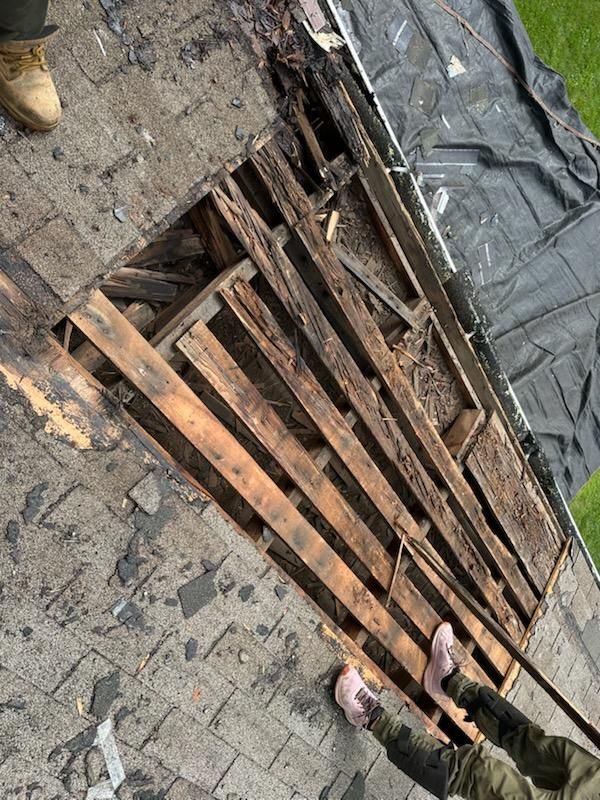Rotted roof section removed, showing damaged wooden planks. Person's feet visible.