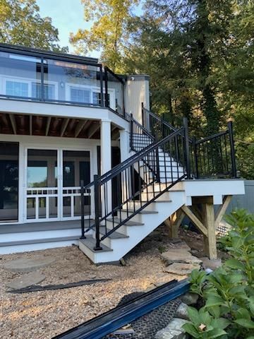 Two-story house with black metal staircase and railing leading to a deck; gray siding, white trim; trees in the background.