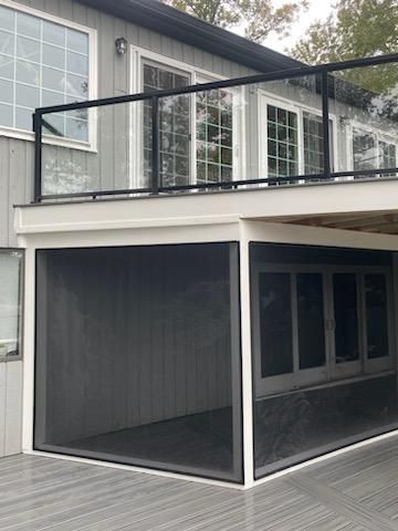Gray house with a screened-in porch below a glass-railed deck.