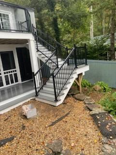 Black metal railing surrounds outdoor stairs and deck. Gray and white steps with gravel ground.
