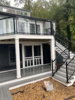 Multi-level deck with black railing and glass panels, gray and white exterior, stairs leading up.