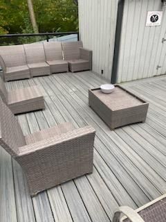 Outdoor deck with gray wicker furniture: couches, armchairs, coffee table with a bowl.