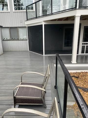 Outdoor deck with grey flooring, a chair, and a screened-in porch area.