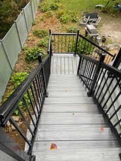 Outdoor wooden stairs with black railings leading down to a yard.