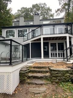 Two-story gray house with decks and glass railings overlooking steps made of rock.