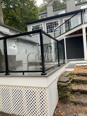 Deck with black railing and glass panels, overlooking stairs. Gray house in the background.