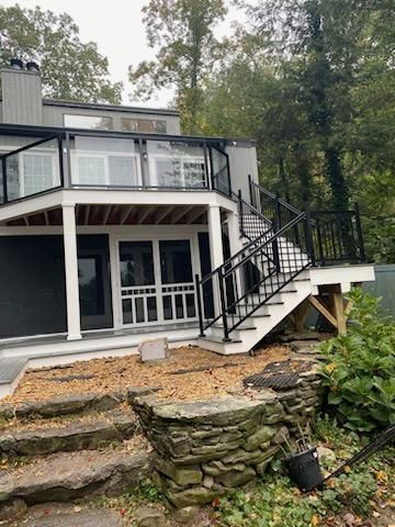 Two-story home with deck and stairs, black railings, white trim, gray siding, and stone steps.