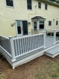 Deck with gray flooring, white railing, and a light yellow house.