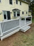 Gray deck with white railing, steps leading to backyard. House with bay window in the background.