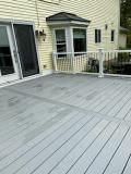 Gray composite deck with a sliding door, bay window, and white and black railing.