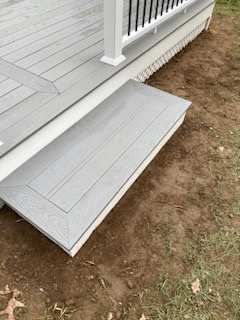 Gray composite deck with a single step, against a grassy, dirt yard.