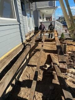 Men rebuilding a porch with exposed wooden beams. House exterior with blue siding.
