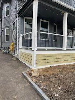 Gray house with a porch featuring white railings and horizontal wood paneling.