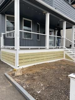 Gray house with white porch, railing, and new wooden base. A person stands on the porch.