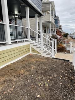 A house with a white porch and steps, beige siding, and brown soil in front.