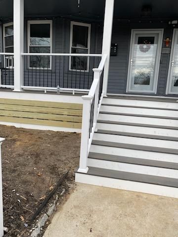 Gray and white steps leading up to a front door with a white railing. The house is gray.