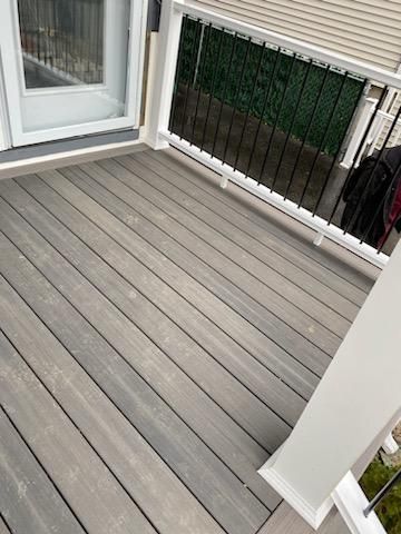 Gray composite deck with white railing, overlooking greenery, next to a white door.