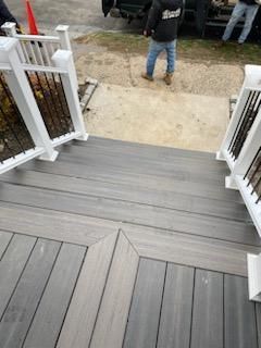 Grey composite deck with stairs and white railing. Person in background.