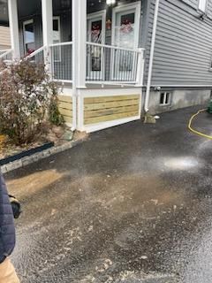 Asphalt driveway being pressure washed in front of a house with a porch and wooden siding.
