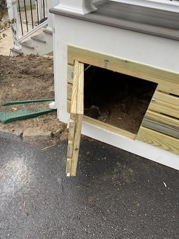 Wooden access door ajar in a white wall near a paved road. Soil and stairs are visible.