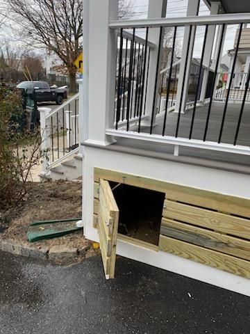 Wooden storage door under a white porch with black railing; street in the background.
