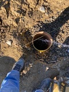 Person's feet near a circular hole in the ground; a string is stretched across the opening.