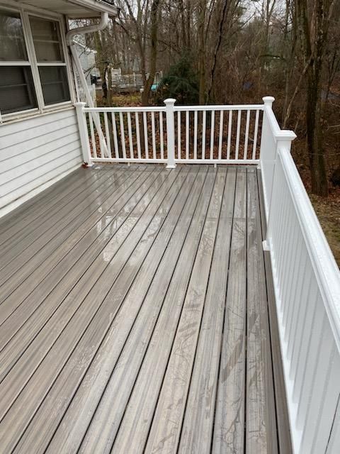 Gray wooden deck with white railing, next to a white house.