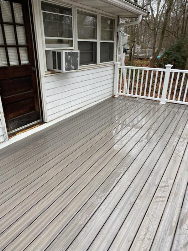 Gray composite deck outside a white-sided house with a dark wooden door and white railing.