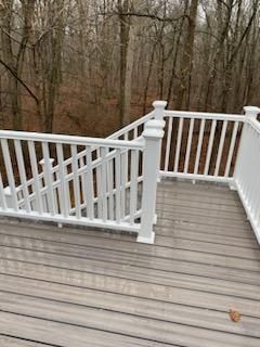 White railing on a wooden deck with stairs leading down to a forest setting.