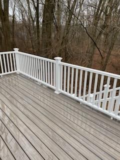 A deck with white railing overlooks a forest. Gray deck boards are wet.