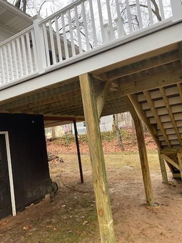 A wooden deck with white railing, supported by green posts. Underneath is a shed and stairs.
