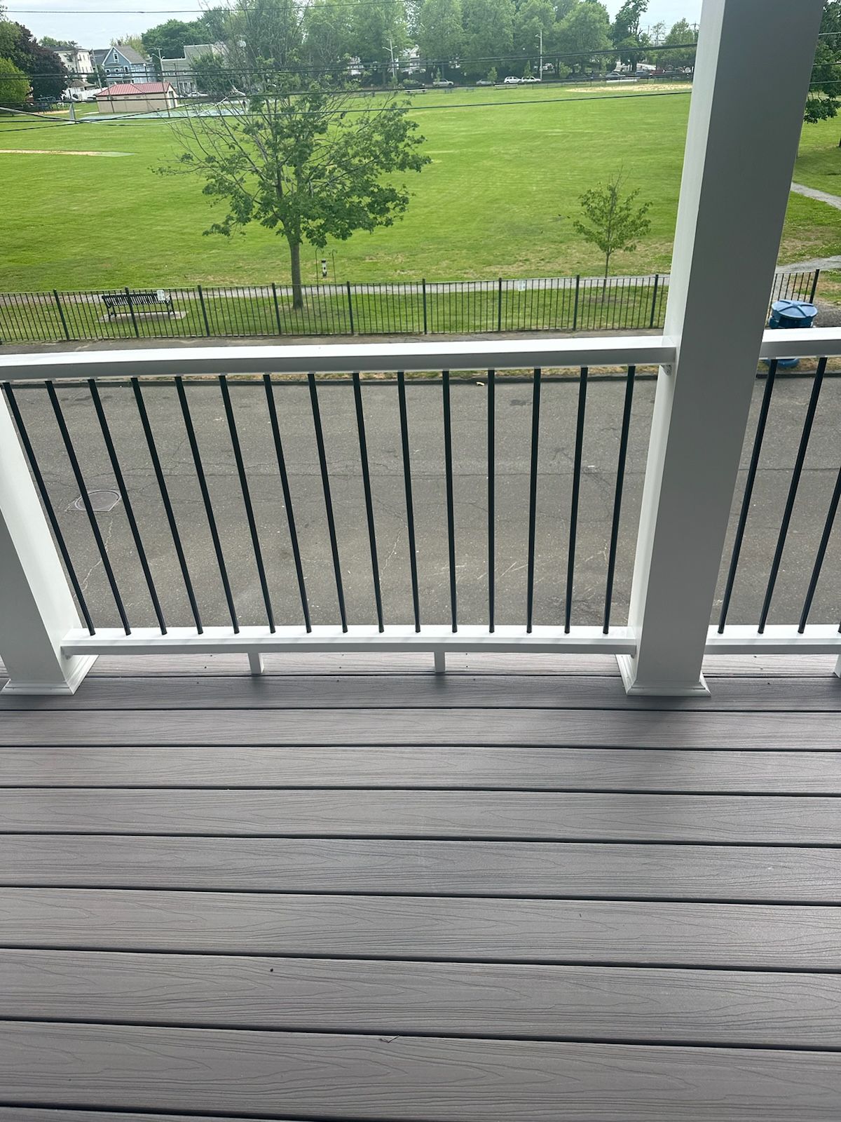 Deck with gray planks, black railing, and view of green field.