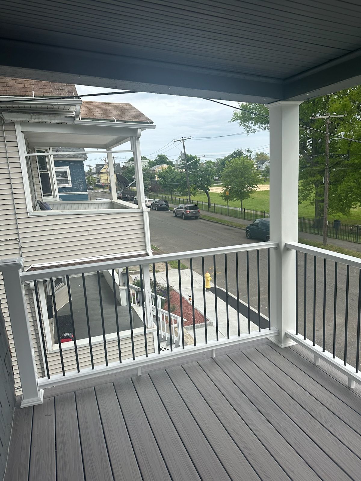 Balcony with gray decking, white railing, and view of street, park, and houses.