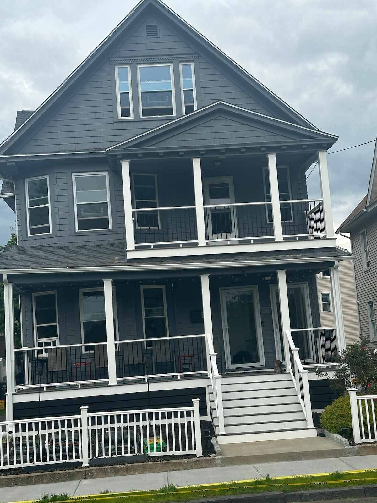 Three-story gray house with white porch railings and stairs.