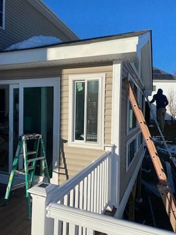 Exterior view of a house addition with siding, a window, and a deck. A person is on a ladder.